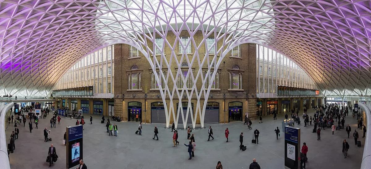 Wide interior view of the western departure hall at London King's Cross station with many people under a lattice roof.